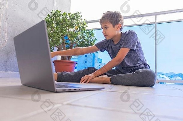 男孩拿着笔记本电脑做运动，在阳台上练习瑜伽。运动、健康生活方式、积极休闲、家庭娱乐
