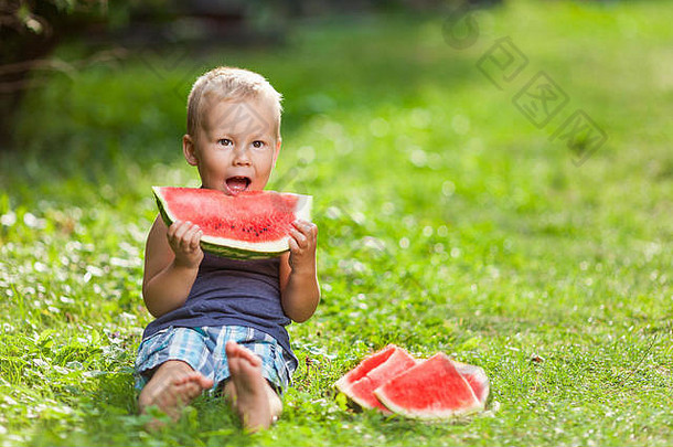 可爱的蹒跚学步的孩子坐在户外吃着一片西瓜