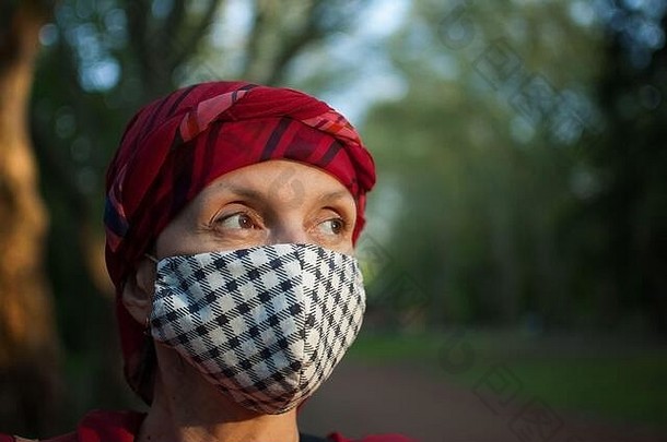由于冠状病毒的影响，在阳光明媚的春天，公园里的成年妇女戴着手工织物面罩作为配饰和保护元素