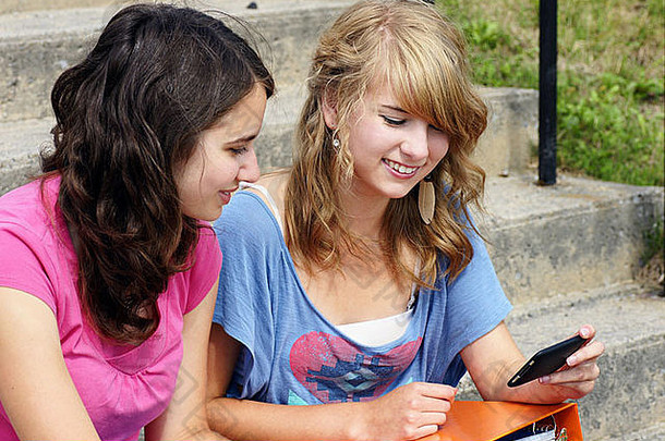 两个年轻的青少年学生用手机笑着，非常适合社交、社交媒体等。
