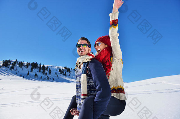 这对年轻夫妇在雪上玩得很开心。山上的快乐男人背着他微笑的女朋友。