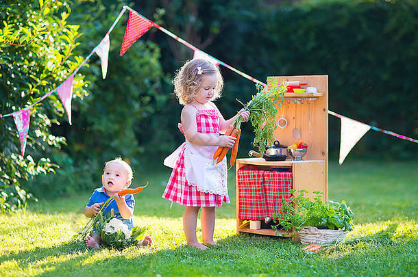 孩子们在玩玩具厨房。孩子们在夏季花园里玩耍。男孩和女孩在bac烹饪和烘焙健康蔬菜