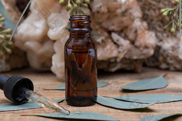 琥珀色圆形玻璃瓶中的桉树精油，带有玻璃滴管和木质背景上的新鲜桉树叶。植物疗法。