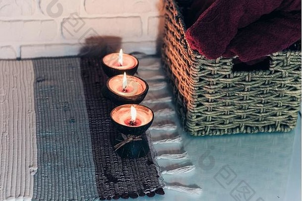 在白色墙壁对面的编织多彩地毯和柳条盒上燃烧椰子壳中的spa aroma蜡烛，舒适的家庭内部