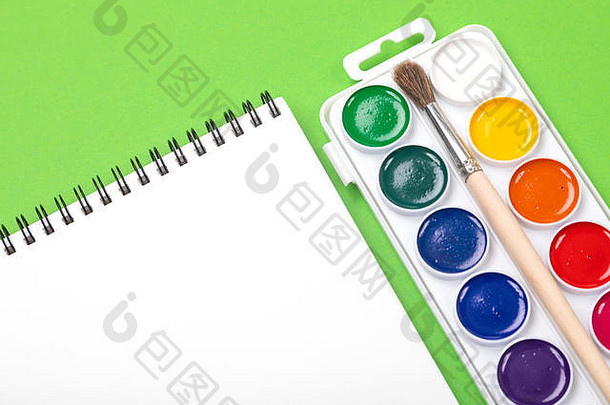水彩颜料和画笔，带有画册，用于在绿色背景俯视图上独立绘制