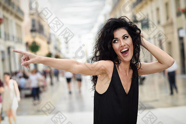浅黑肤色的女人有趣的女人穿休闲衣服指出手指街年轻的女孩卷曲的发型站城市背景
