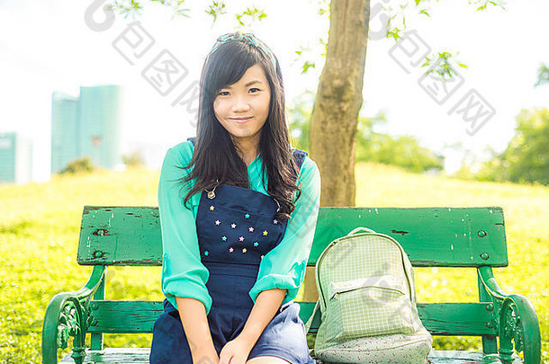 长椅上坐着迷人的年轻亚洲女人，公园里的美丽女孩夏日肖像
