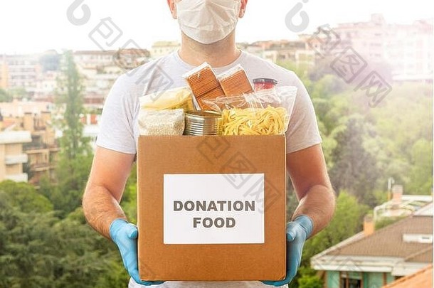 捐款箱。运送食物。志愿者食物帮助。一个戴着口罩和医用手套的男人在街上拿着一盒食物