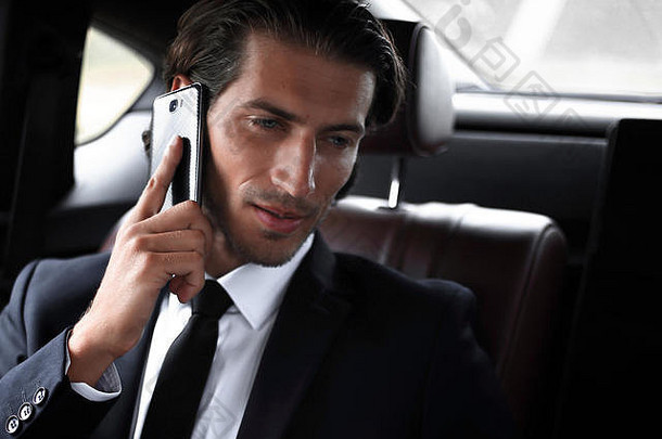 英俊的商人在车里用手机。