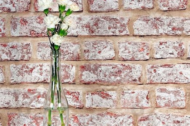 白色喷雾康乃馨在一个小玻璃瓶与旧砖墙效果的背景