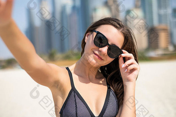 在迪拜的JBR海滩上，一位穿着泳装的年轻美女在自拍。夏日度假时，年轻漂亮的女游客在海滩上进行旅游自拍
