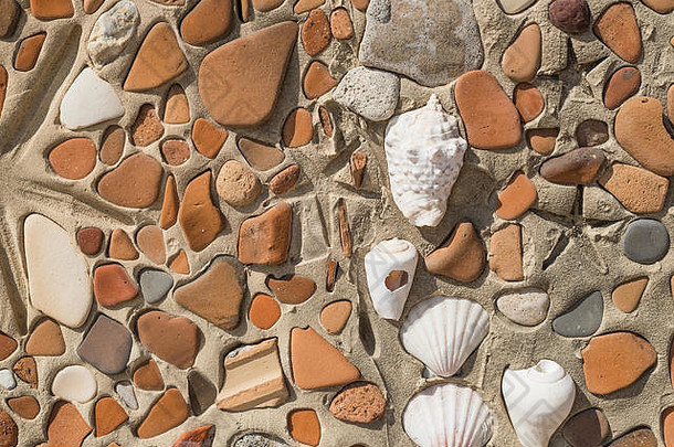 古代文化概念-彩色碎块石和贝壳镶嵌背景特写照片。建造时混凝土中的壳体模式