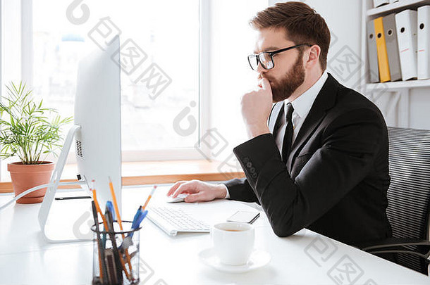 图片集中年轻的有胡子的商人坐着办公室电脑