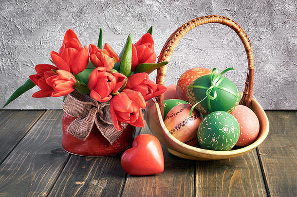 复活节构图，红色郁金香，木制心形，木制背景上有一篮彩色复活节彩蛋