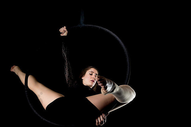 优雅的空中舞者一名女子，她用一个孤立在黑色地板上的<strong>铁环</strong>表演