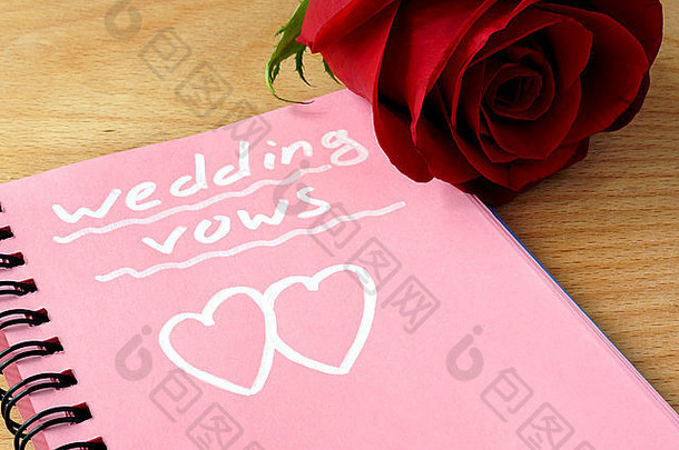木制背景上印有结婚誓言和玫瑰的粉红色记事本。
