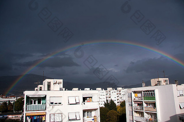 乌<strong>云</strong>密布的深蓝色天空中城市建筑上方的彩虹