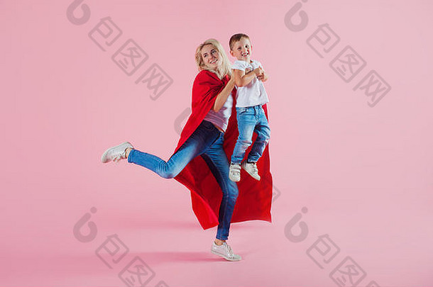 <strong>妈妈</strong>是个<strong>超级</strong>英雄。有趣的家庭，一个穿着红色斗篷的年轻金发女人和她的儿子跳了起来，粉色背景