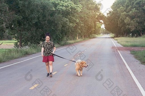 一名亚洲妇女带着她的金毛猎犬在公路上行走。