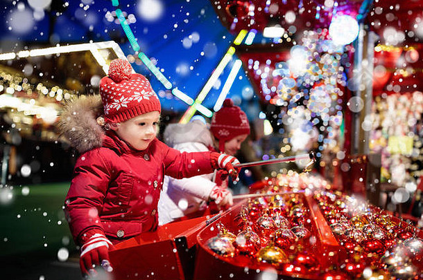 孩子们在传统的圣诞集市上。下雪的夜晚，孩子们和圣诞节集市。家庭购物圣诞礼物和礼物。男孩和女孩玩钩子游戏