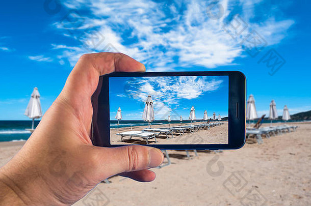在阳光明媚的海滩上手持智能手机拍照