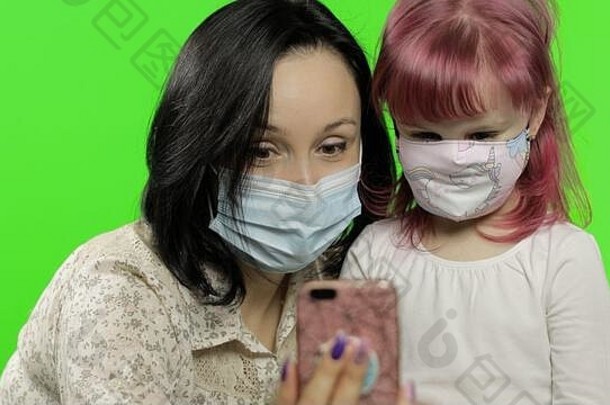 母亲、女儿戴着口罩，手持<strong>手机</strong>在视频通话。社会距离，冠状病毒COVID-19保护概念。可爱的小孩喜欢使用智能<strong>手机</strong>。社会化媒体。色度键
