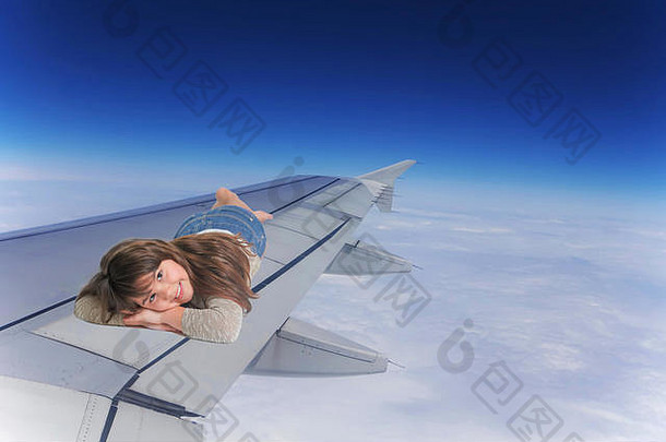 微笑的小女孩躺在飞行中的飞机机翼上。蓝色的天空和云是背景。