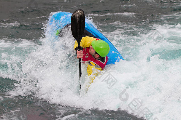 在白水中划皮艇的年轻男子。这名男子正在表演翻滚，周围溅起了汹涌的水花。