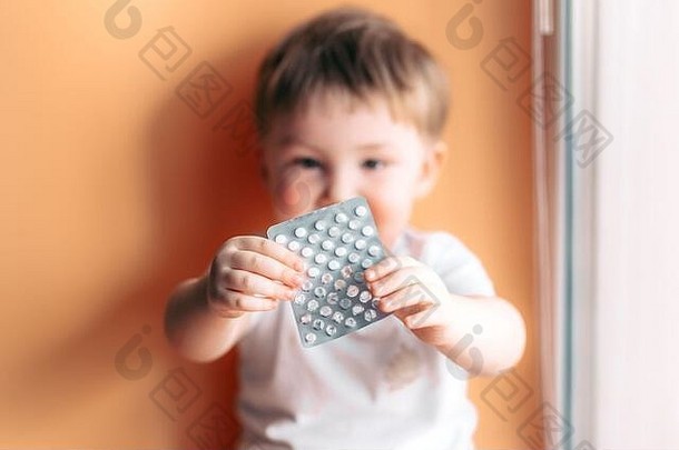 一个蹒跚学步的小男孩手里拿着一个盘子，盘子里有药片，他选择了药片的焦点，孩子没有集中注意力