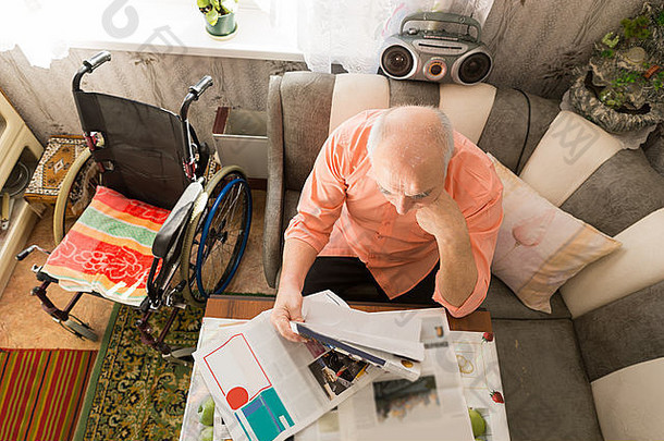 客厅桌子边上坐着轮椅，严肃的秃顶老人正在<strong>阅读小报</strong>的鸟瞰图。