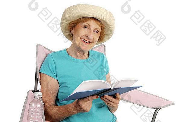 一位漂亮的年长女士坐在沙滩椅上休息，手里拿着一本<strong>好书</strong>，书被隔离在白色的地板上