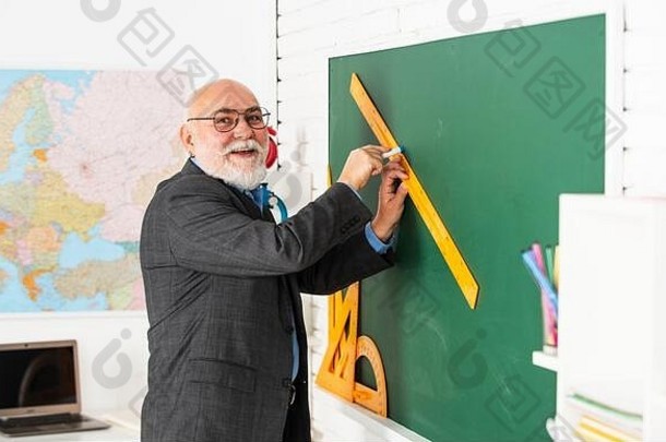 练习时间。教师戴眼镜的人用尺子在黑板上画画。回到学校。你从什么角度看。几何形状。高中现代教育。高级男教师在绘图时使用尺子。