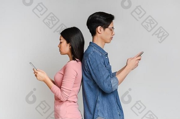 亚洲女孩和男孩背靠背站在一起，使用手机