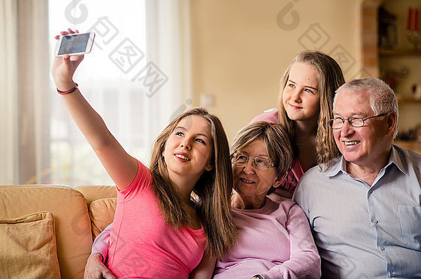 十几岁的女孩在沙发上用手机拍摄自己、姐姐和祖父母的<strong>照片</strong>
