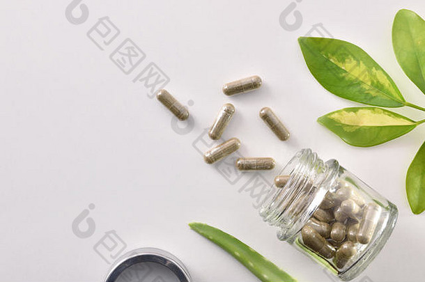 天然药物胶囊装在敞开的玻璃罐中，放在白色的桌子上，上面有芦荟和植物叶子。自然医学概念。顶视图。水平复合