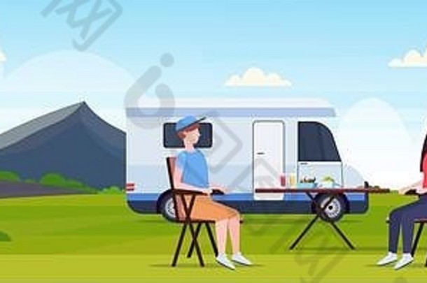 这对夫妇坐在露营地附近的桌子旁，家庭拖车、卡车、大篷车、汽车女女花时间在他们的暑假理念——美丽的自然景观上