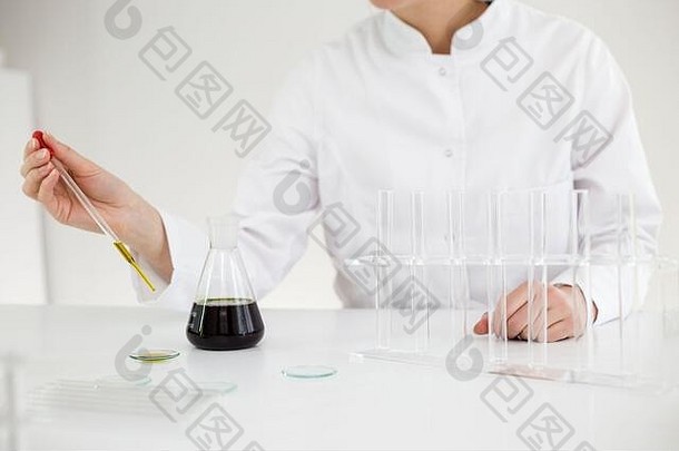 戴着眼镜的女科学家在<strong>手表玻璃</strong>上测试从植物中提取的cbd油。她用一个<strong>玻璃</strong>滴管和一个碗做实验