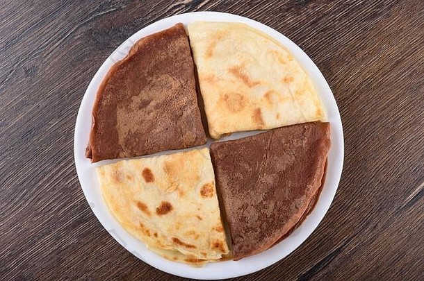 平铺。薄煎饼是纯的，加了可可粉。在木制背景上的白色盘子上煎饼。传统的俄罗斯早餐。