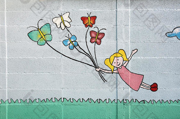 可爱的金发女孩和蝴蝶在混凝土砌块墙上的草地上漂浮