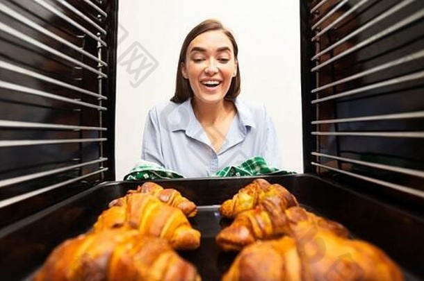 快乐的女人采取美味的脆皮羊角面包烤箱
