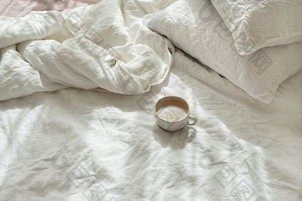 在床上喝一杯新鲜的咖啡，早晨的心情。亚麻棉纺织床上用品。有机和天然亚麻。舒适的卧室内部。美丽的灯光。