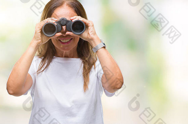 一位中年西班牙裔妇女站在孤立的背景下用双筒望远镜观察，脸上带着幸福的表情，脸上带着自信的微笑，露出微笑