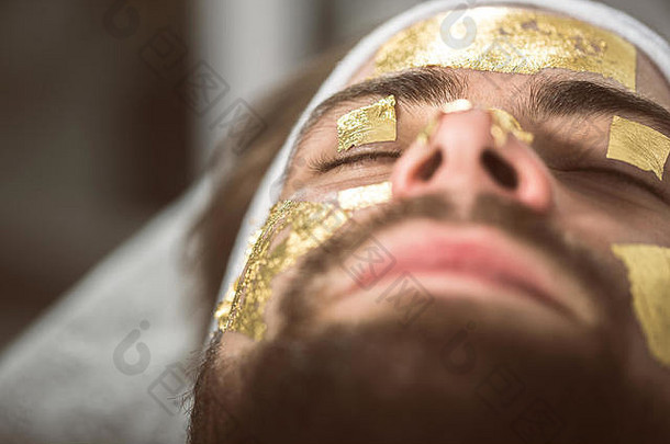 美容师应用金面具叶子男人的脸