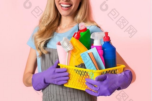 重点放在清洁用品篮子上。穿着围裙和紫色橡胶手套的家庭主妇