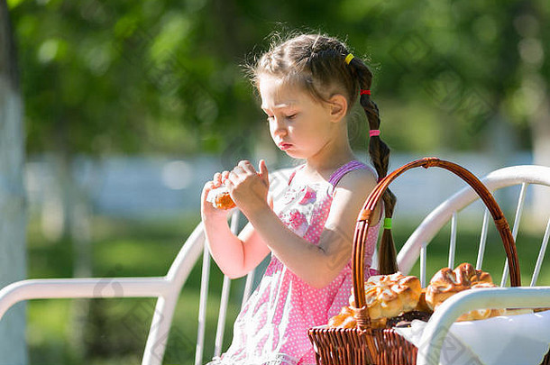 一个小女孩正坐在一个城市公园里，手里拿着一篮子面包和面粉做的面包。