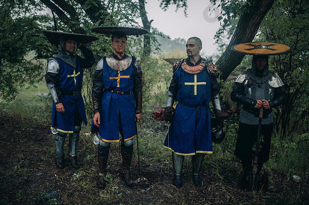 四个年轻人的形象是中世纪的十字军骑士，身穿盔甲，在他们的盾牌下<strong>躲雨</strong>。