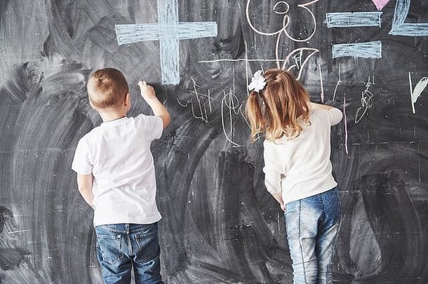 可爱的小女孩和男孩用蜡笔在墙上画画。儿童作品。可爱的小学生在黑板上写字