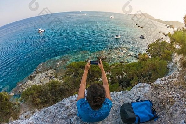 年轻的女人背包坐着悬崖前面海洋智能手机ponza岛海岸意大利