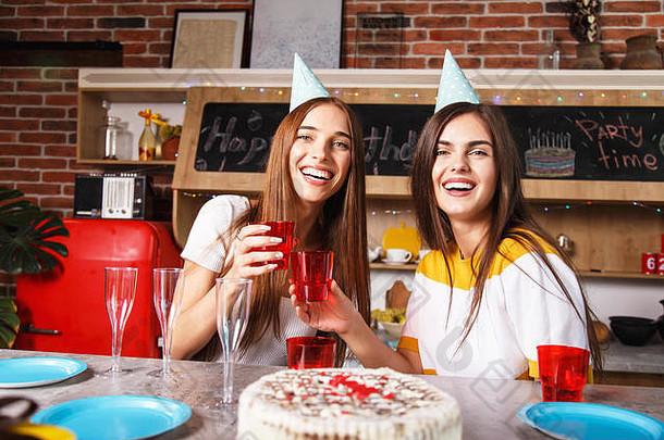 两个很棒的女朋友在派对上，戴着帽子，举起酒杯，面带微笑