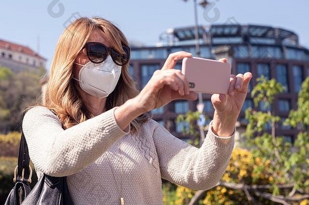 在冠状病毒大流行期间，一名成年妇女在观光时戴着口罩，并用手机拍照。